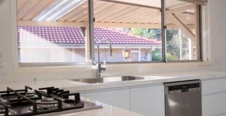 Modern kitchen interior with gas stove, stainless steel sink, and large window overlooking a tiled roof and garden.