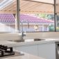Modern kitchen interior with gas stove, stainless steel sink, and large window overlooking a tiled roof and garden.