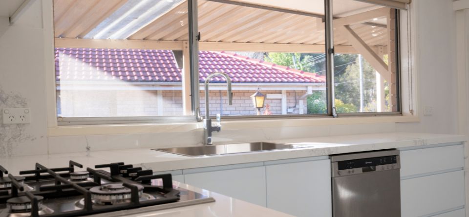 Modern kitchen interior with gas stove, stainless steel sink, and large window overlooking a tiled roof and garden.