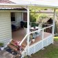 Covered outdoor deck with white railing, wooden flooring, and outdoor furniture including a blue sofa, white chairs, and dining table.