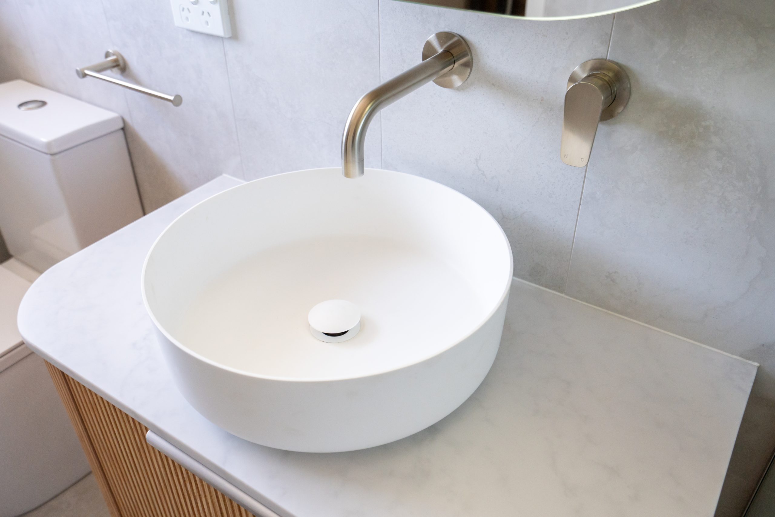 Stylish round white bathroom sink with wall-mounted faucet on a marble countertop next to a toilet.