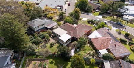 Aerial view of suburban houses with gardens, backyards, and a nearby parking lot surrounded by trees.