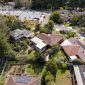 Aerial view of suburban houses with gardens, backyards, and a nearby parking lot surrounded by trees.