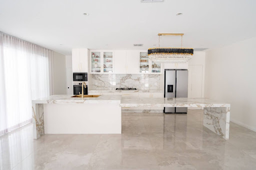 Luxury modern kitchen with marble island, gold pendant chandelier, integrated appliances, and glossy tiled flooring