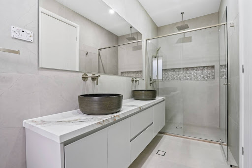 Modern bathroom with double vessel sinks, marble vanity top, frameless glass shower, and tiled feature niche
