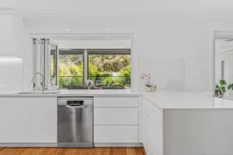 Modern white kitchen with large window and dishwasher.
