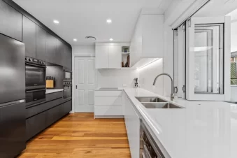 Modern kitchen with dark cabinets, white counters, and timber flooring.