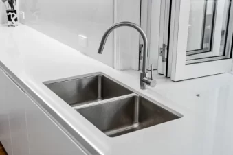 Double stainless steel sink with modern faucet on white countertop.