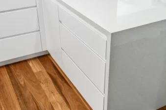White kitchen cabinets with stone countertop and timber flooring.